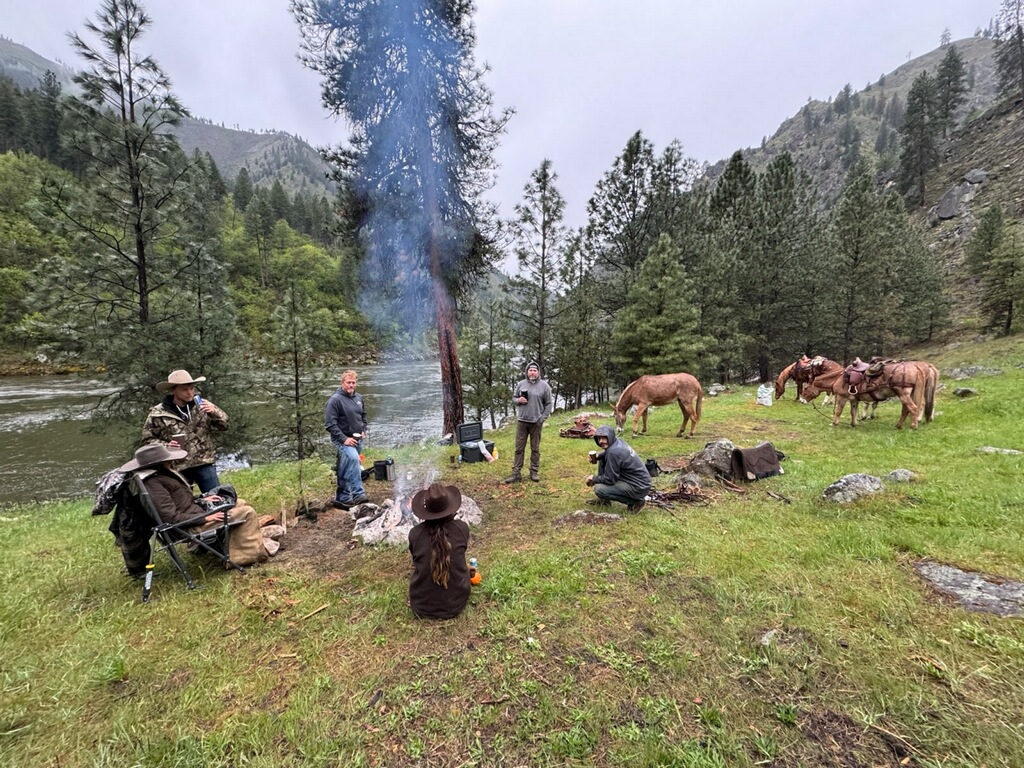 Backcountry camp at Shepp Ranch on the Salmon River Idaho with group around campfire and horses grazing in remote wilderness setting